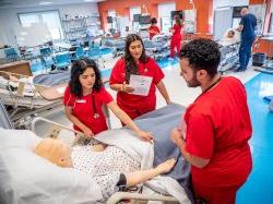 Nursing students around practice dummy in hospital bed